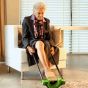 Ältere Frau sitzt auf einem Stuhl und benutzt die Steve Complete Anziehhilfe, um ihre Stützstrümpfe selbständig anzuziehen